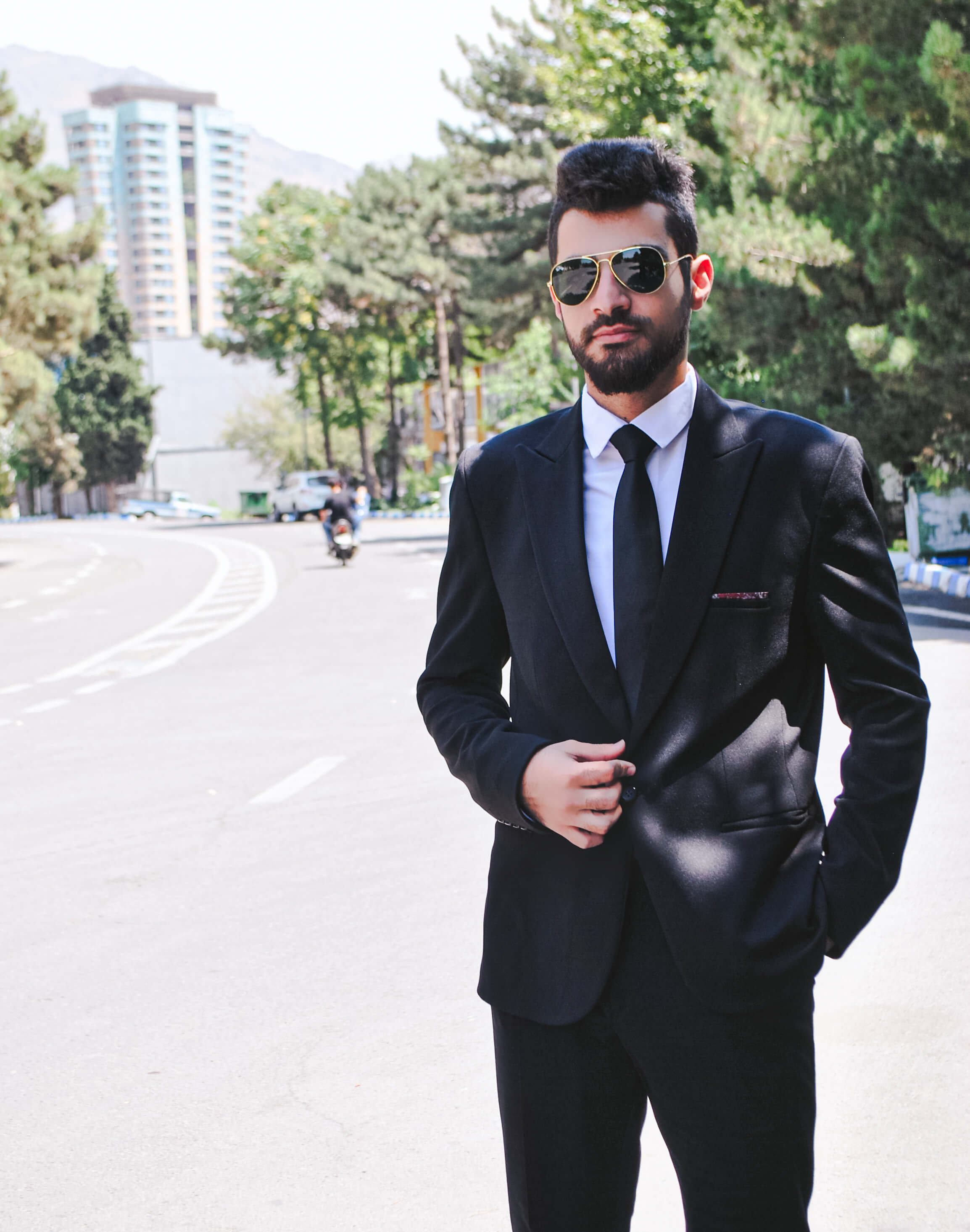 «مجتبی جاهد با کت‌وشلوار مشکی و عینک آفتابی در خیابانی شهری»